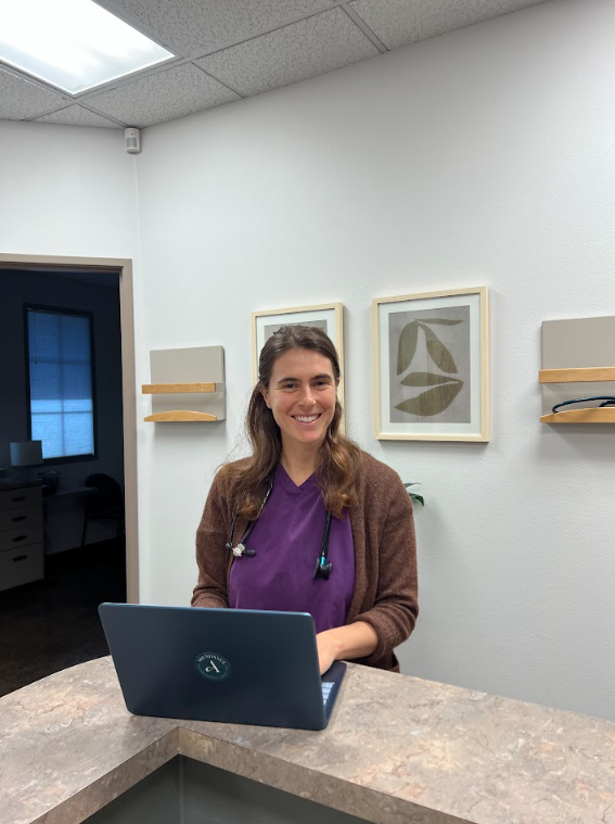 A doctor in purple scrubs smiling at the front desk with a laptop
