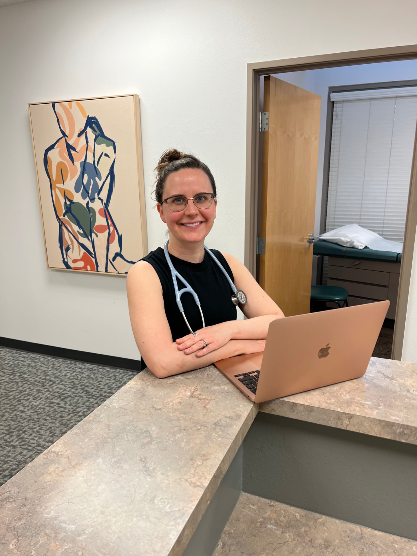 Dr. Gusching smiling at the front desk with a laptop beside an exam room