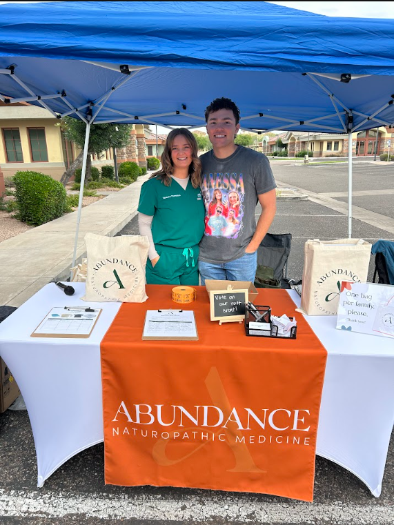 Two community event volunteers behind the orange Abundance welcome table